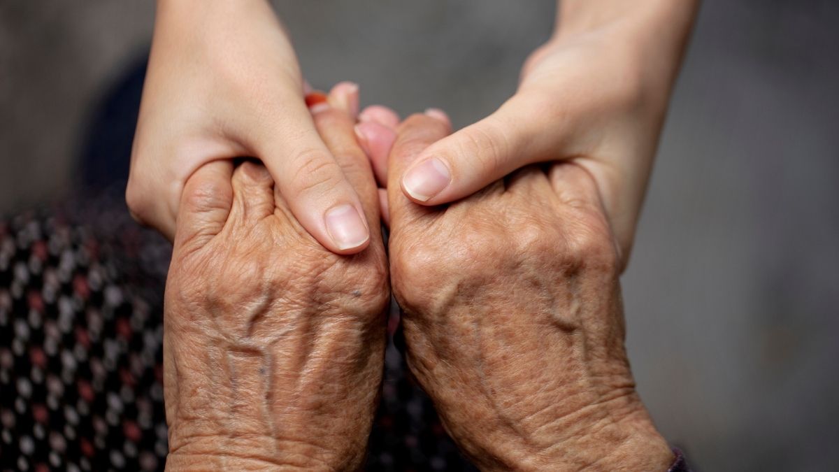 Middle-aged woman helping her elderly parents at home, symbolizing the cost of caregiving.